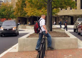 Pedestrian stepping over a short fence in a broad traffic median