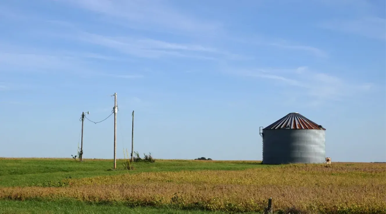 Photo of a field with a grain storage bin and power line poles