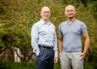 2 people standing together with a green landscape behind them