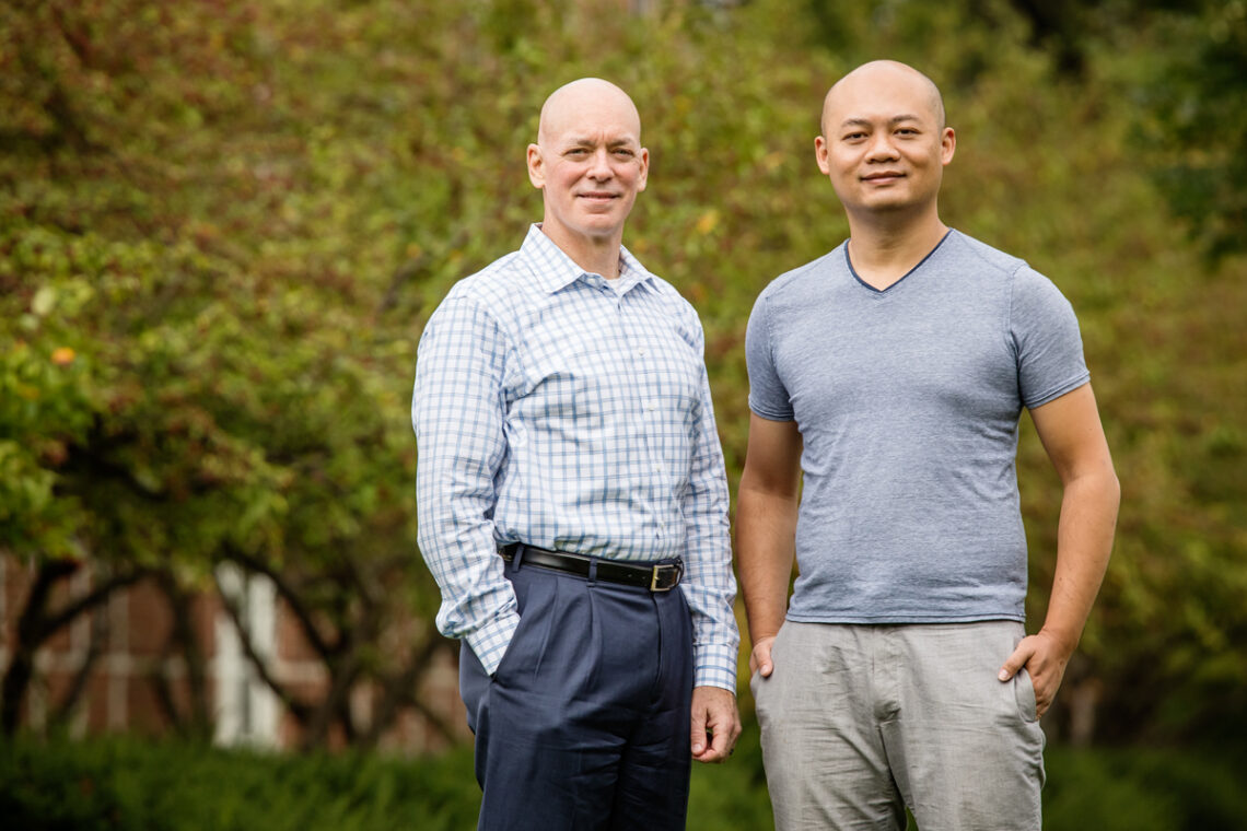 2 people standing together with a green landscape behind them