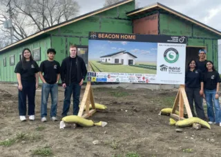 Students standing next to the the Beacon project poster in front the house: Chambana Today