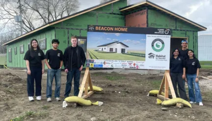 Students standing next to the the Beacon project poster in front the house: Chambana Today