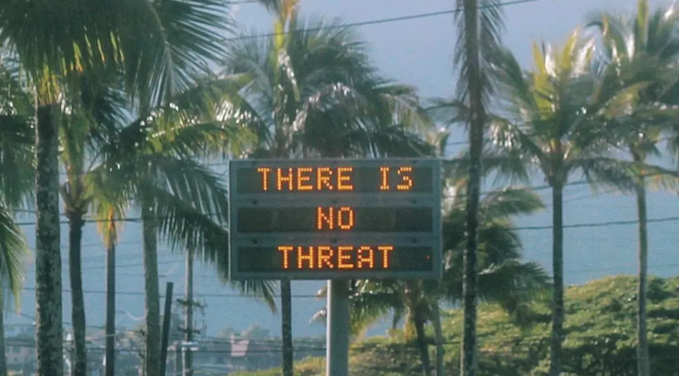 View of a digital sign along a palm tree-lined road in California showing the phrase "THERE IS NOT THREAT""