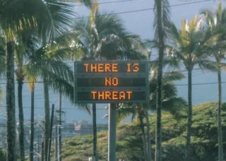 View of a digital sign along a palm tree-lined road in California showing the phrase "THERE IS NOT THREAT""