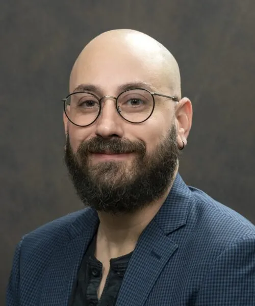 Photo of a man with glasses and a beard wearing a blue blazer