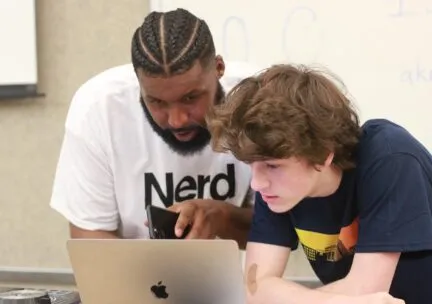 Professor Lamont Holden shows a student how to use software on a laptop