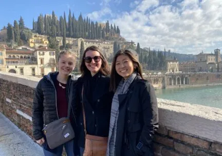 3 students stand on a brdige facing a large river