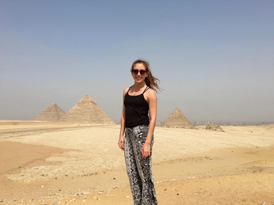 Person standing in the middle of a desert with pyramids in the background