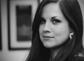 person with long hair looks at the camera with a sly smile, the image is in black and white