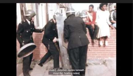 A still image from the film Handsworth Songs. A group of three white policemen equipped with shields and helmets surround someone. Behind them on a brick wall three Black people are sitting. The captions at the bottom of the image read “[muddy distortion ripples beneath mournful, howling notes]”.