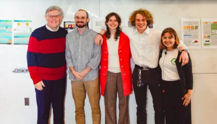 5 people stand with arms around each other and projection screen above them