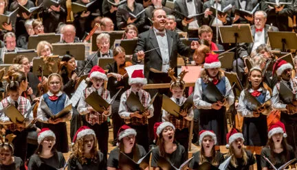 many people standing and singing with conductor holding baton in the middle