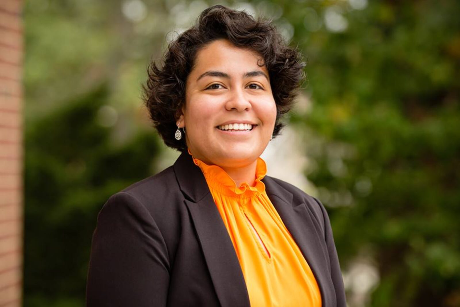 person wearing orange shirt and black jacket smiles