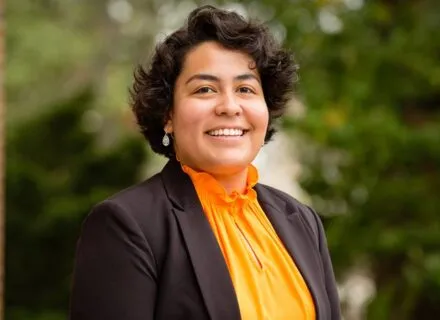 person wearing orange shirt and black jacket smiles