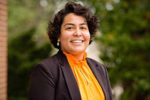 person wearing orange shirt and black jacket smiles