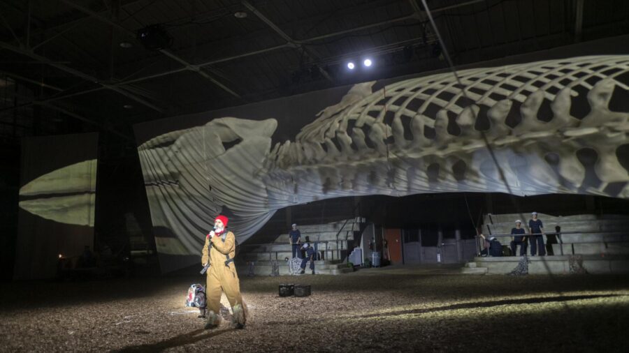 cetacean performance showing large whale skeleton and deke weaver on a mic wearing a red hat