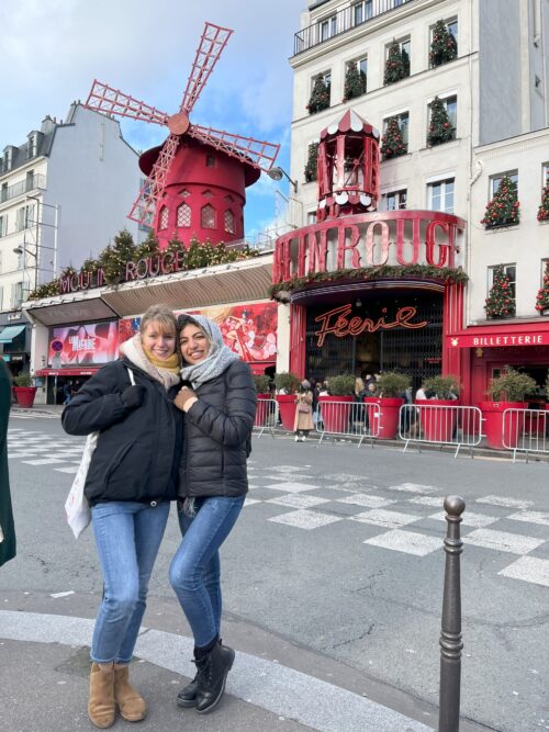 two students in coats stand by the moulin rouge in Paris France