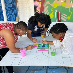 3 artists lean over table painting together