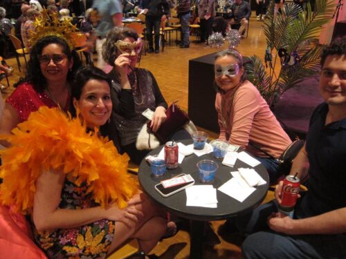 people dressed in bright colors and masks sit around a table smiling
