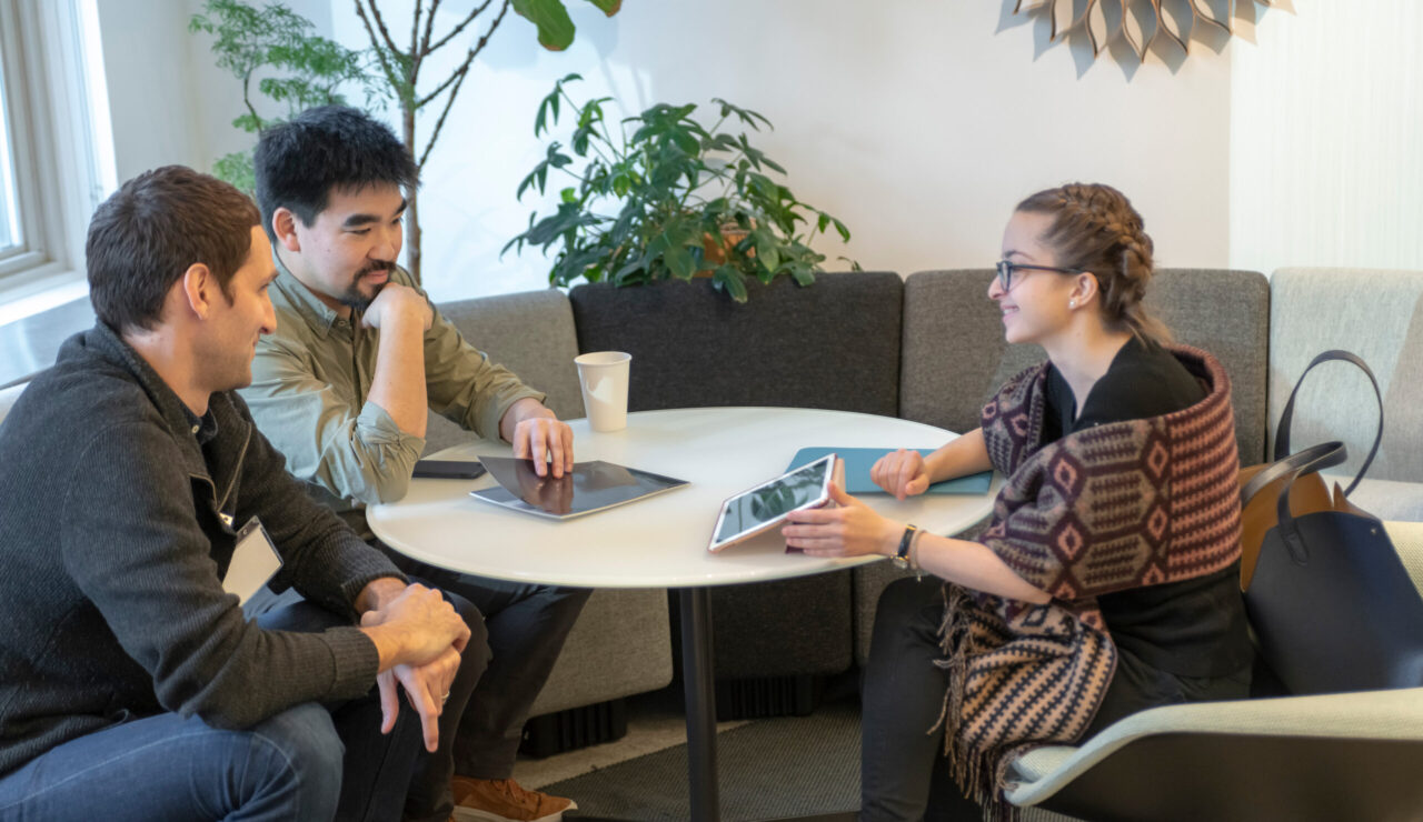three people sit at a round table for a portfolio review by tablet