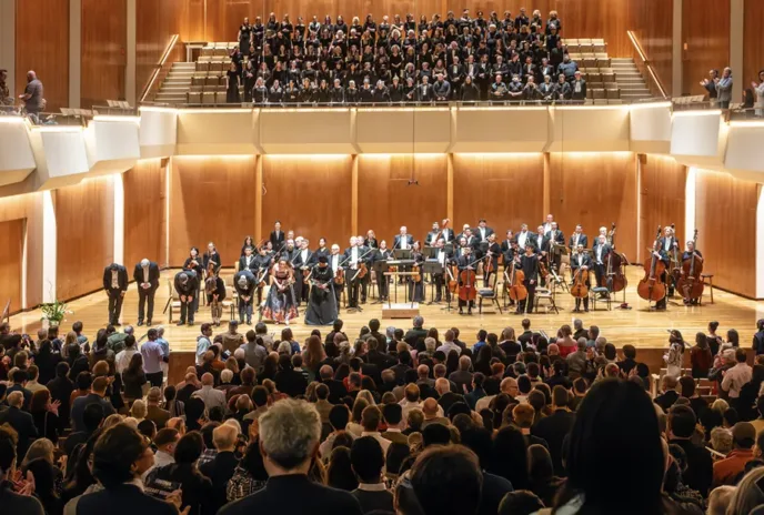 many people performing onstage in a concert hall orchestra with full audience watching