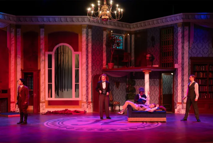 stage set that looks like a luxurious early 20th century home drenched in pink and purple lighting with actors onstage