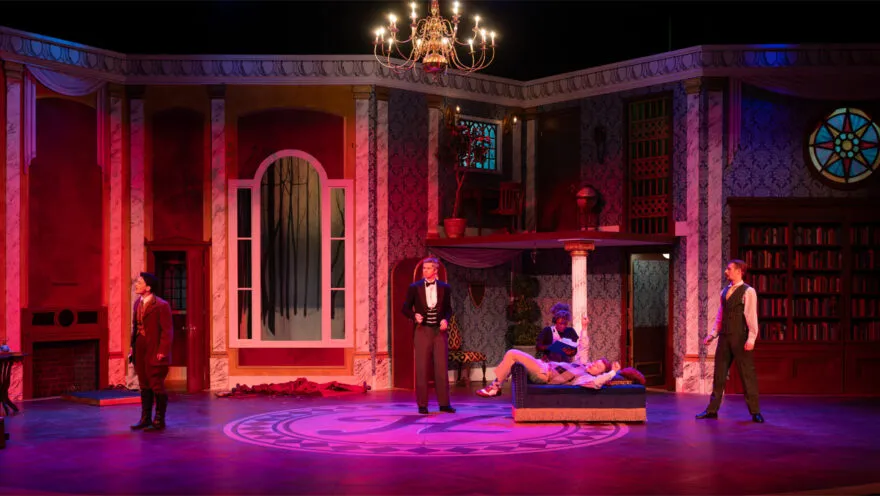 stage set that looks like a luxurious early 20th century home drenched in pink and purple lighting with actors onstage