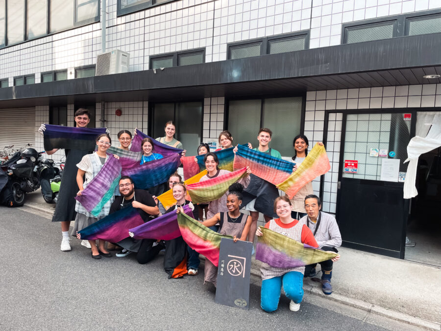 15 people holding up colorful fabric on small street