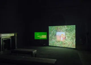 a dark gallery with screens showing green grasss surrounding a photograph and a green screen with text