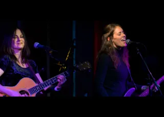 two people play guitars and sing into mics