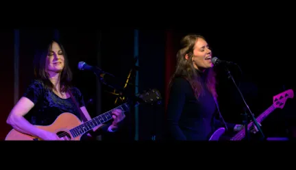 two people play guitars and sing into mics