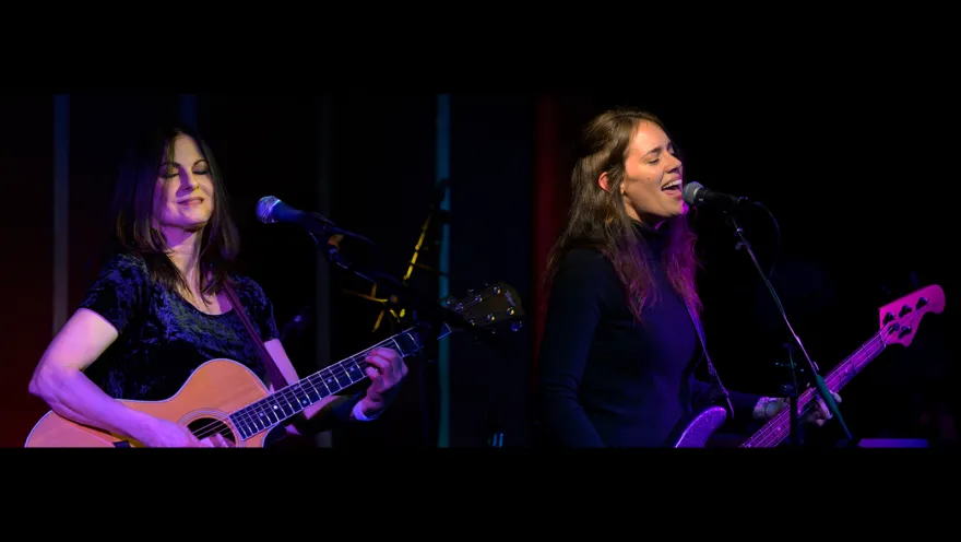 two people play guitars and sing into mics