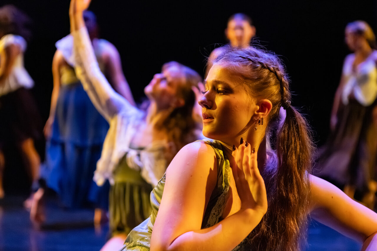 one dancer in foreground on floor with hand raised and earnest look
