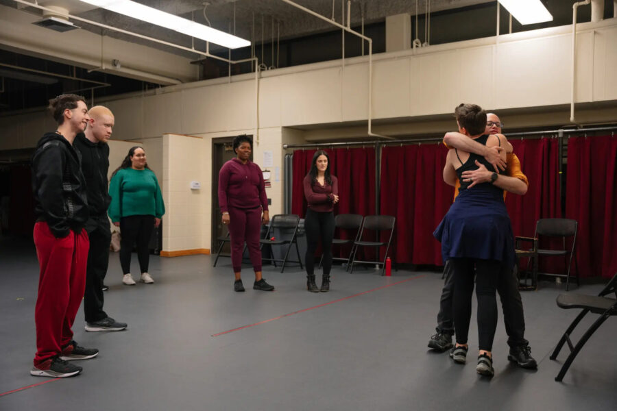people in a rehearsal room, two are hugging while others watch
