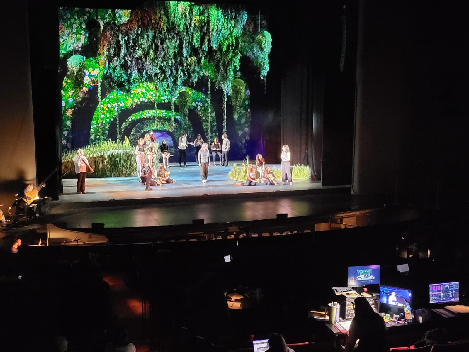 a proscenium theatre with actors onstage and tech folks running sound and lights in the booth