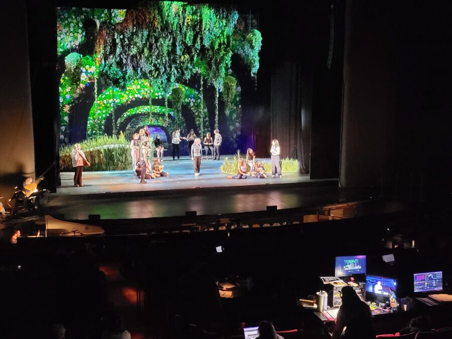 a proscenium theatre with actors onstage and tech folks running sound and lights in the booth