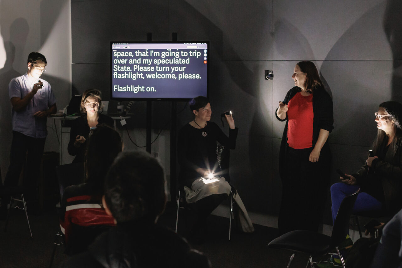 several people holding flashlights in a dark room with a lit up screen with text