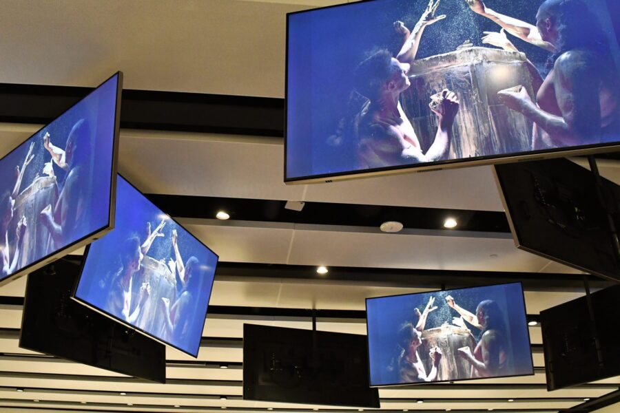 several large screens suspended from the ceiling shows images of live performance