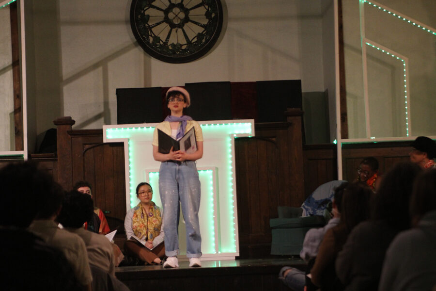 an actor speaks while standing center stage with a book in hand
