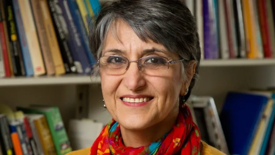 Photo of Dr. Miraftab in front of a bookshelf wearing a yellow sweater with a red scarf