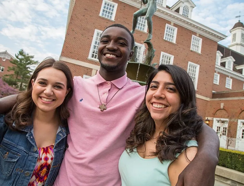 three smiling students standing together in front of university buiding