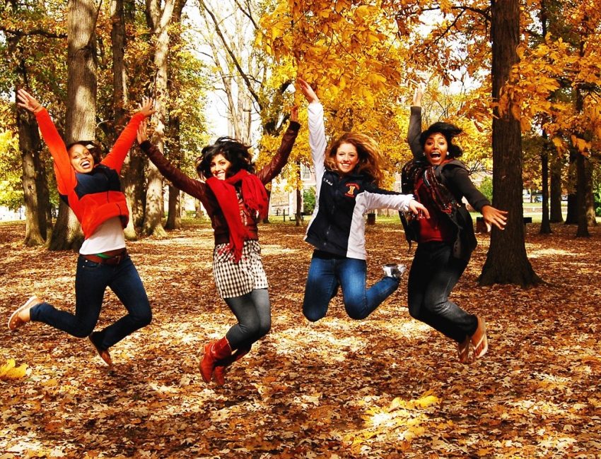 four students jumping in the fall leaves