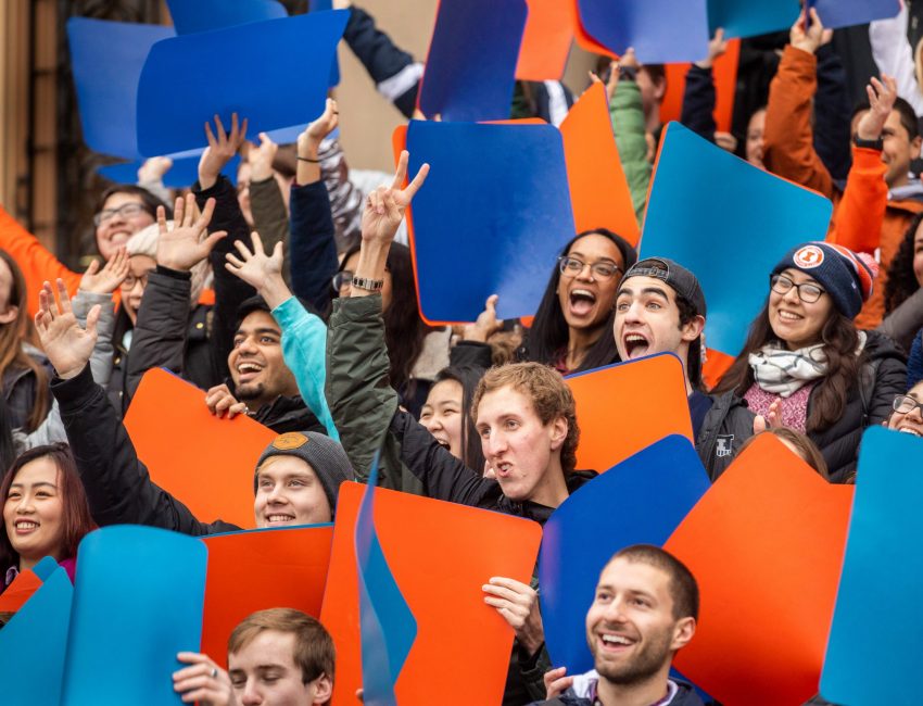 smiling students at event holding orange and blue signs