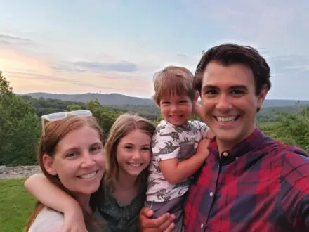 Family photo in front of green trees and hills on the horizon.
