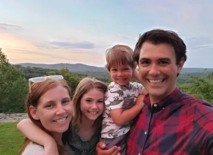 Family photo in front of green trees and hills on the horizon.