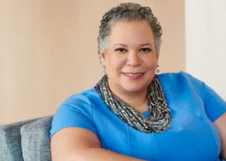 Photo of Dr. Edwards sitting on a chair with a blue blouse against a beige wall