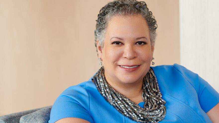Photo of Dr. Edwards sitting on a chair with a blue blouse against a beige wall