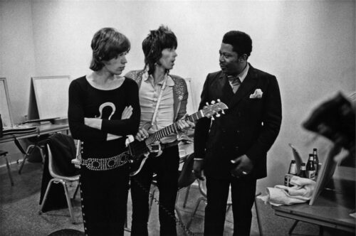 Black and white photo of Mick Jagger, Keith Richards and B.B. King . Keith Richards is holding a guitar as he talks to B.B. King.