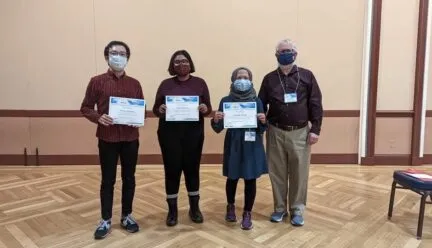 Photo of four graduate student winners of GIS poster competition in meeting room