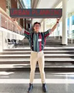 Photo of Colton Johnson on steps in TBH holding an Urban Planning sign over his head